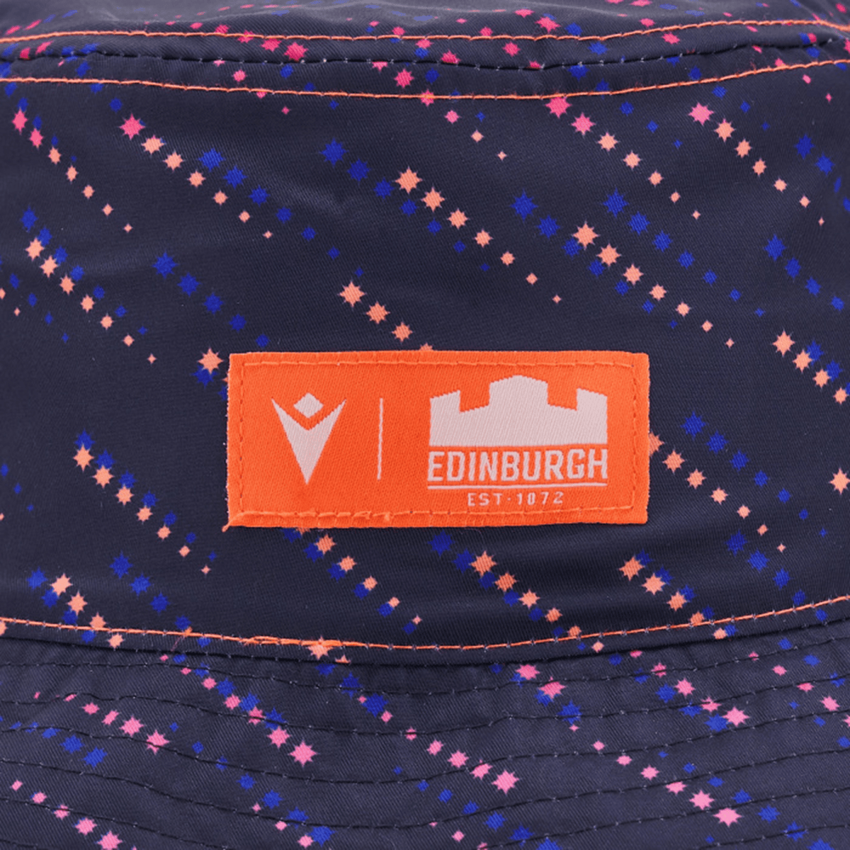 Close-up of the Edinburgh 24/25 Bucket Hat by Macron in navy, featuring pink and blue star patterns. It includes an orange patch with "Edinburgh," "Est. 1872," and the Edinburgh Rugby logo by Macron.