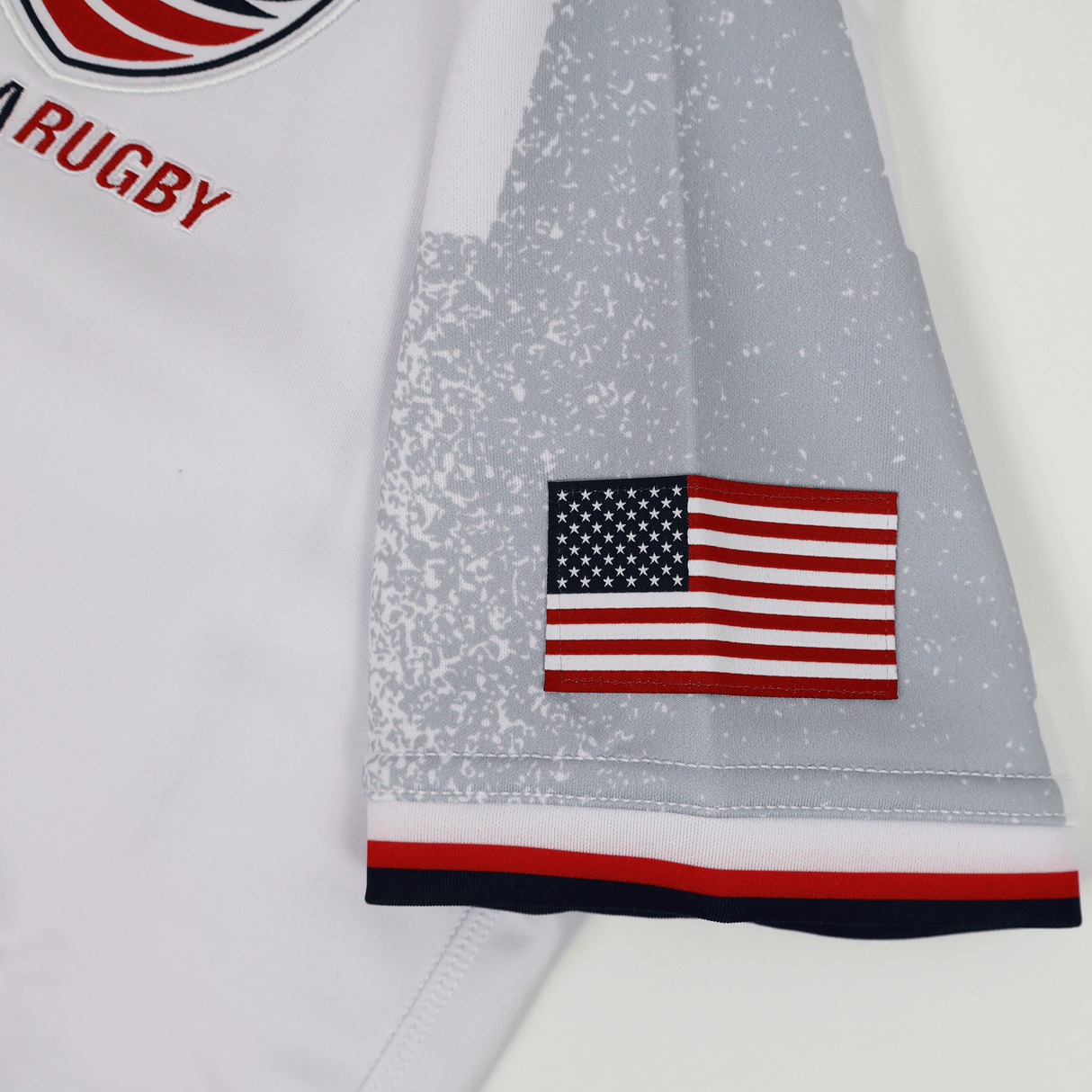 Close-up of the Women's USA Rugby WRWC 25 Away Bodyfit Shirt by Macron, showing a sleeve with a small American flag patch and red, white, and blue trim—official 2025 Rugby World Cup gear in Macron's signature bodyfit style.