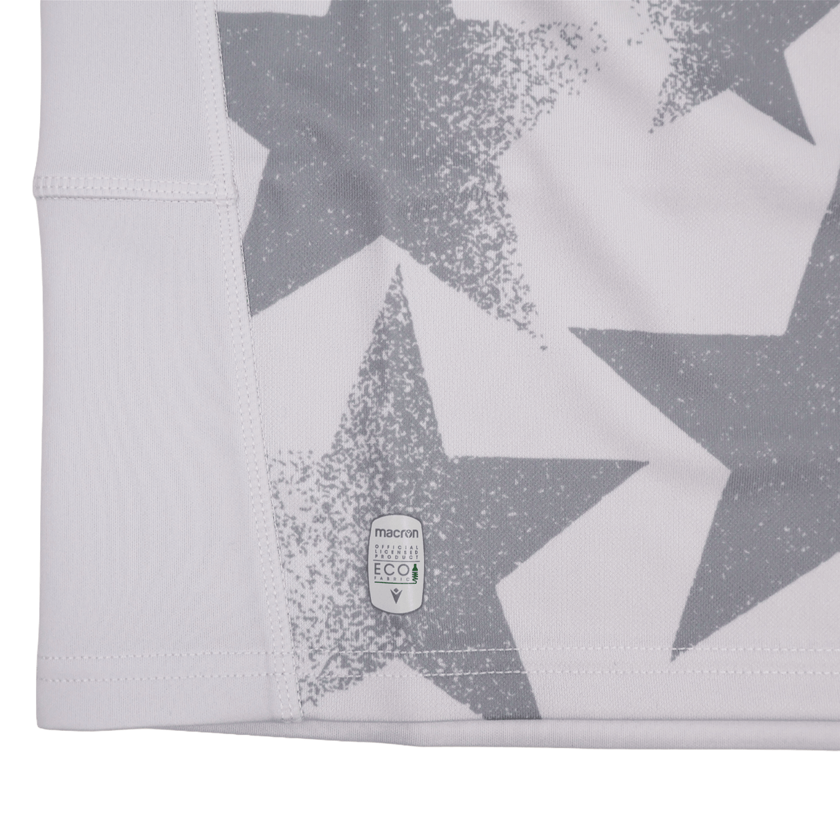 Close-up of a white fabric with large gray stars and a small "macron ECO" label near the hem, from the Youth USA Rugby WRWC 25 Home Jersey by Macron.
