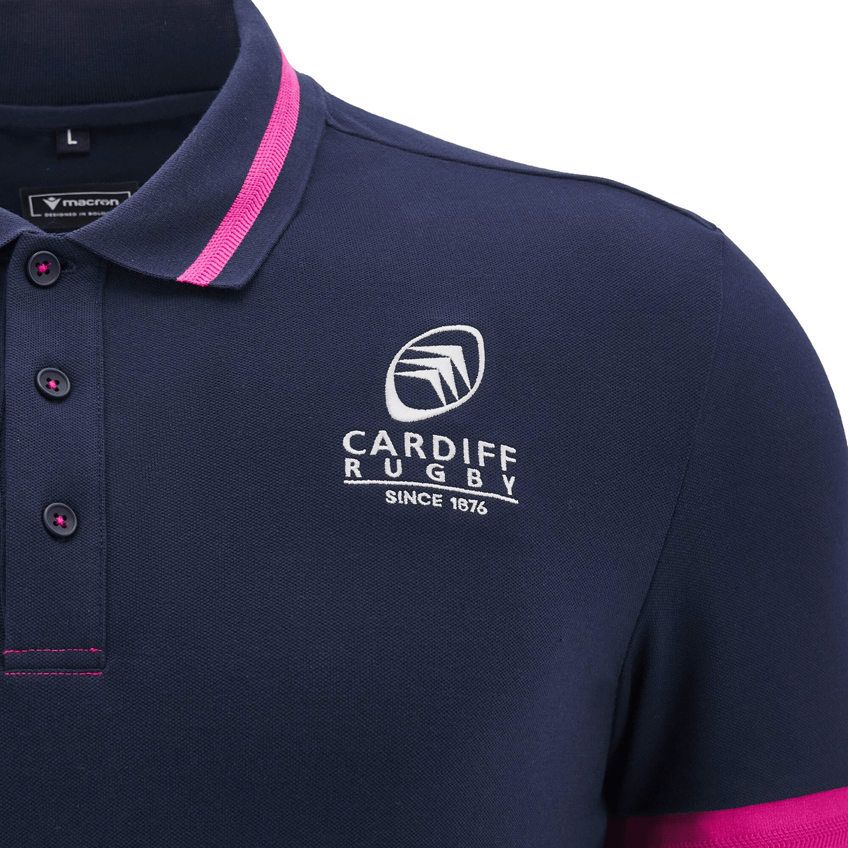 The Cardiff 24/25 Anthem Travel Polo by Macron is a navy polo featuring pink trim, adorned with the iconic Cardiff Rugby logo and "Since 1876" text on the chest, designed for the 24/25 season.