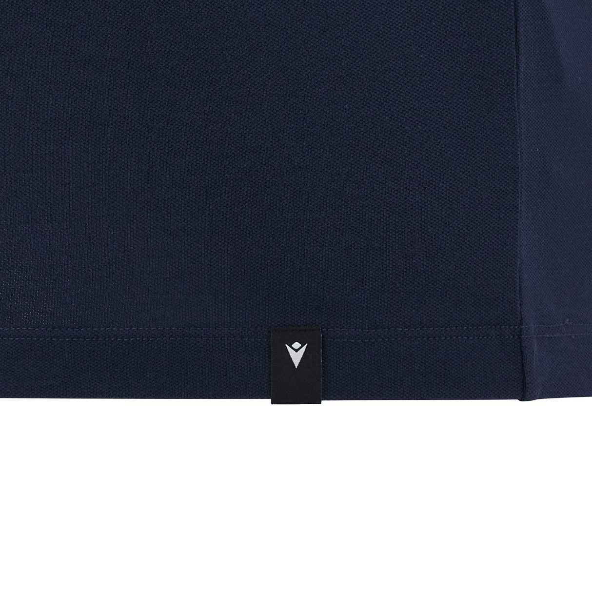 Close-up of the Cardiff 24/25 Anthem Travel Polo by Macron, a navy blue shirt with a small black tag showcasing a white inverted "V" symbol at the hem.