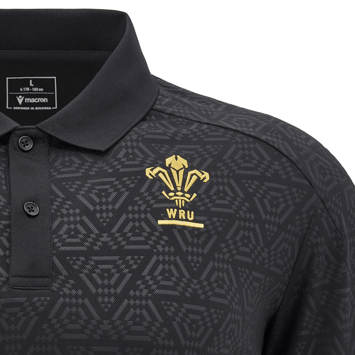 Wales 24/25 Travel Polo by Macron: This black polo shirt showcases subtle geometric patterns and features a gold embroidered WRU logo alongside the "Macron" branding on the chest. Blending style with passion, this exclusive edition is perfect for any Welsh rugby fan.