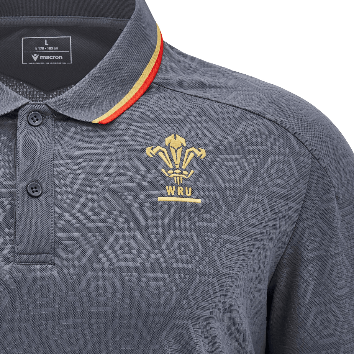 The Wales 24/25 Travel Polo by Macron is a stylish gray polo shirt with a geometric pattern, showcasing the WRU logo in striking gold on the chest and accented with a red and yellow stripe on the collar, making it an excellent choice for representing Wales in style.