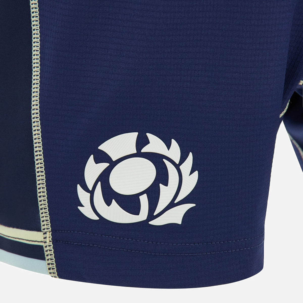 A close-up of blue textured athletic fabric from the Scotland SRU 26/27 Matchday Home Shorts by Macron, featuring a white Scottish Rugby thistle emblem and a reinforced vertical seam with contrast stitching, highlighting the premium craftsmanship of these authentic Macron rugby shorts.