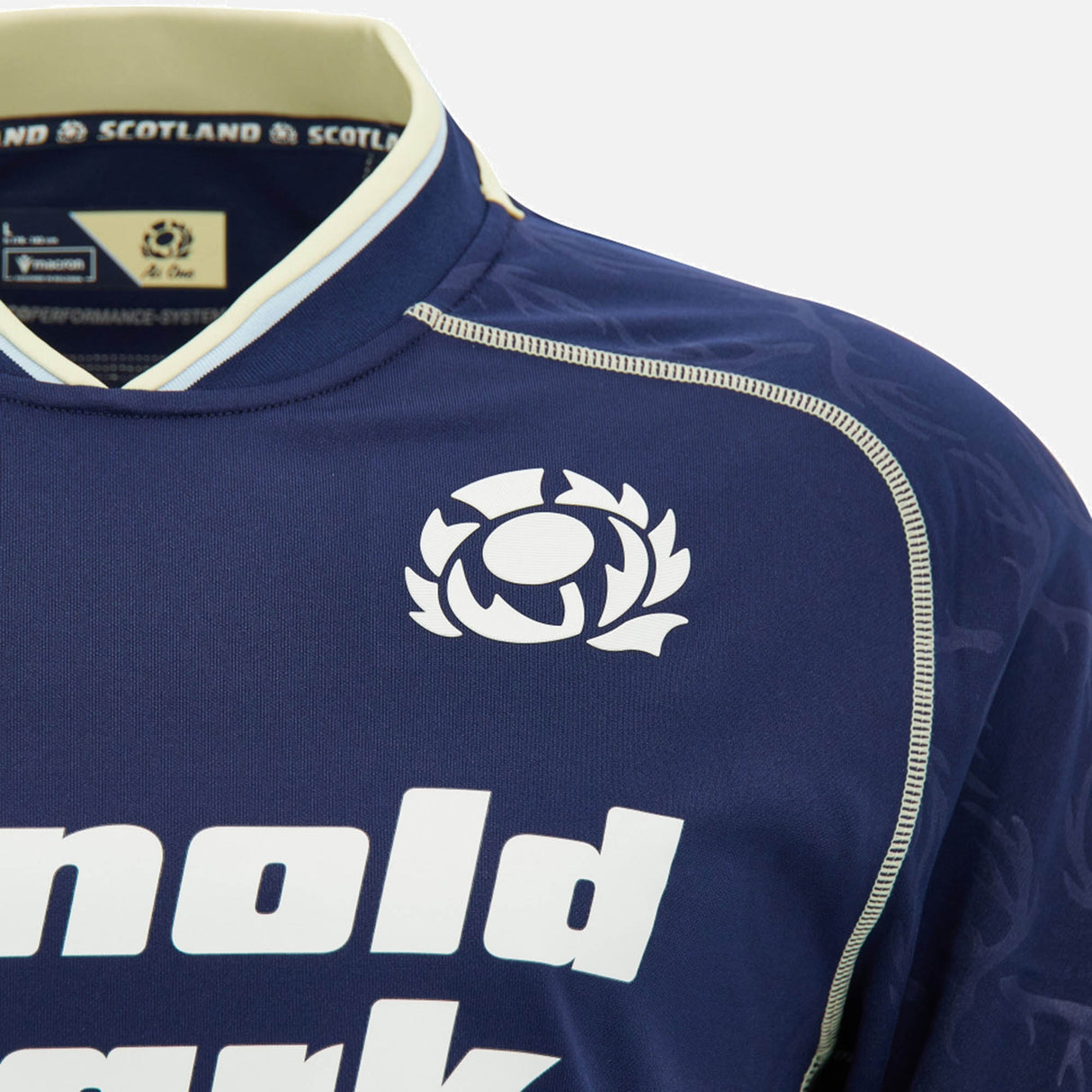 Close-up of the Scotland SRU 26/27 Replica Home Jersey by Macron in navy blue, showcasing the iconic thistle emblem and bold white "Arnold Clark" sponsor text on the front. This official jersey from Macron captures every detail of the classic Scotland rugby design.