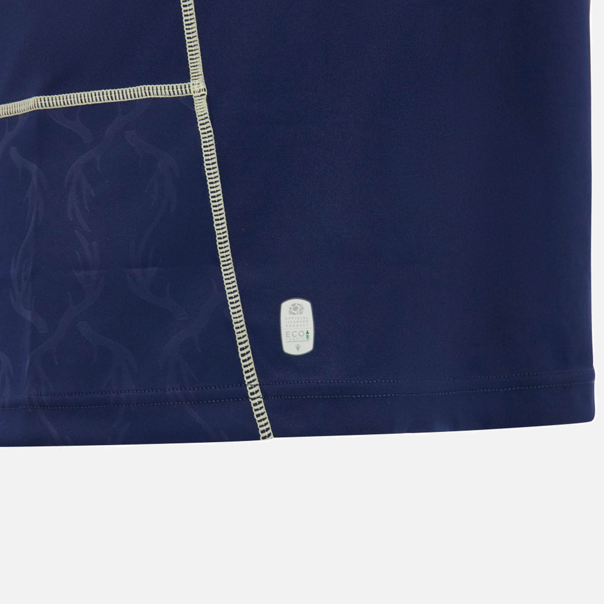 Close-up of a dark blue fabric with light stitching, featuring a subtle pattern and a Macron label near the hem against a white background, reminiscent of the premium craftsmanship found in the Scotland SRU 26/27 Replica Home Jersey by Macron.