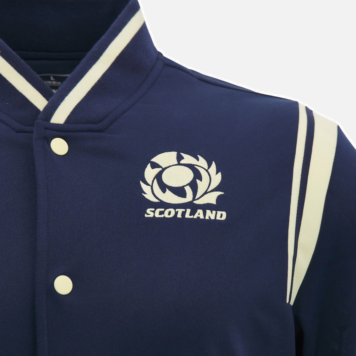Close-up of the Scotland SRU 26/27 Anthem Varsity Jacket by Macron in navy, featuring white stripes and buttons, the official Scotland Rugby logo, and "SCOTLAND" embroidered on the chest. This varsity jacket from Macron highlights top-notch craftsmanship and team pride.
