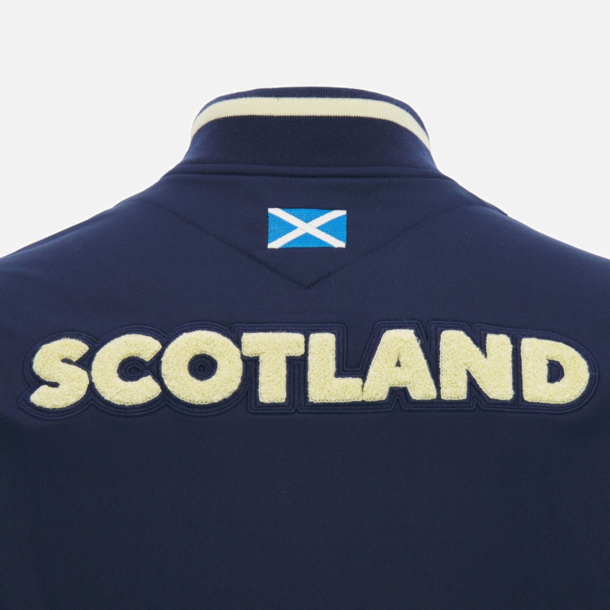 The back of the Scotland SRU 26/27 Anthem Varsity Jacket by Macron showcases "SCOTLAND" in large textured letters with a small Scottish flag above—classic elements that define this navy jacket from Macron.