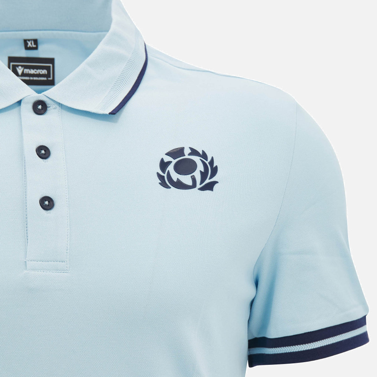 Light blue Scotland SRU 26/27 Travel Polo by Macron featuring navy trim, a three-button placket, and an embroidered thistle emblem on the chest. The inside collar displays the "Macron" brand and XL size label.