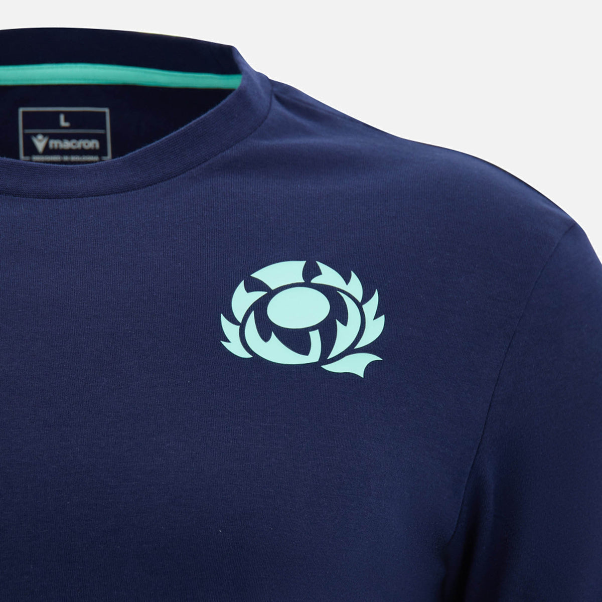 Close-up of the Scotland SRU 26/27 Leisure Cotton T-Shirt by Macron in navy blue, featuring a light blue thistle emblem on the chest and a "Macron" brand label inside the collar, inspired by the official Scottish Rugby Union kit.