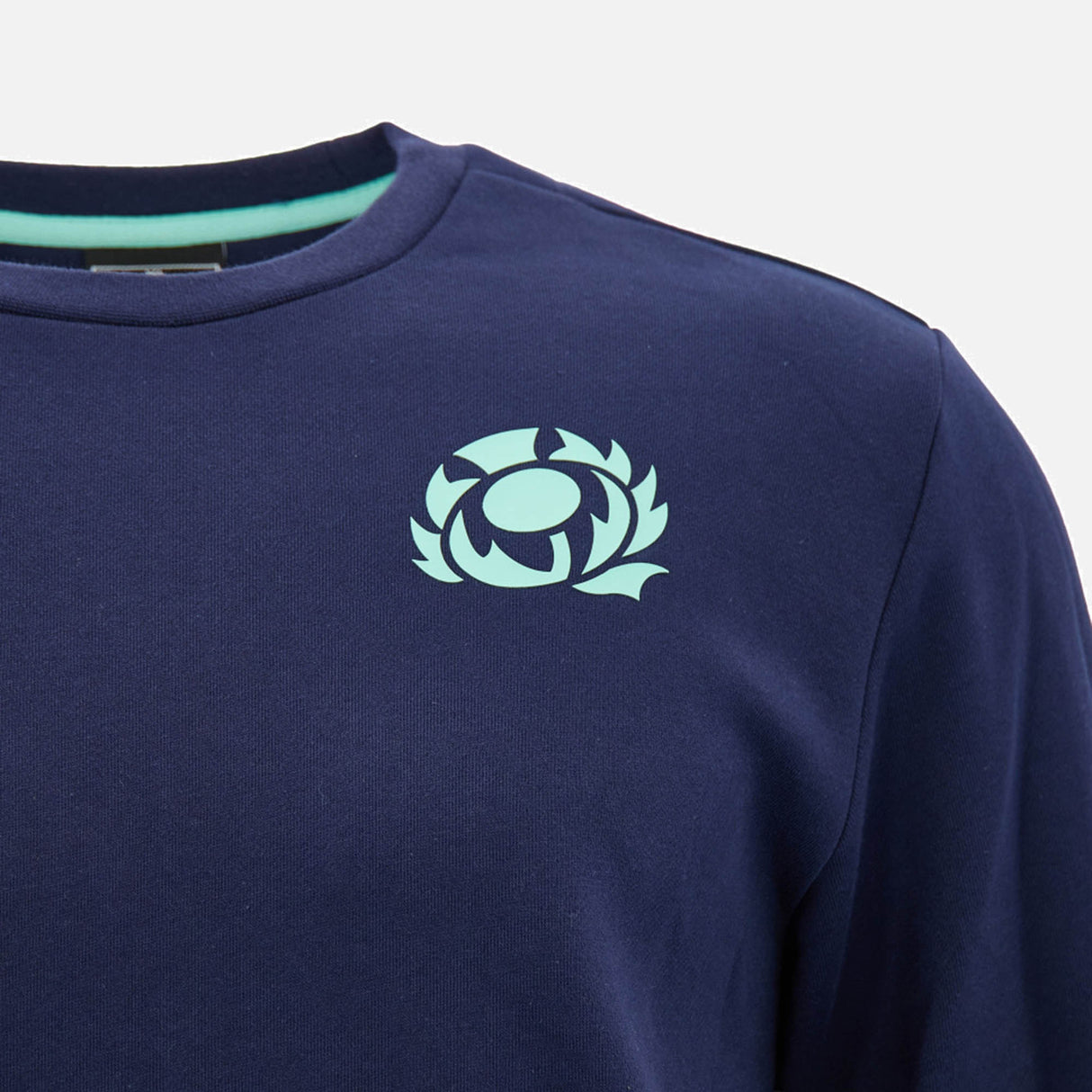 The Scotland SRU 26/27 Leisure Sweatshirt by Macron is a navy blue shirt featuring a light blue stylized thistle emblem on the upper left chest, inspired by classic Scotland Rugby sweatshirt designs.