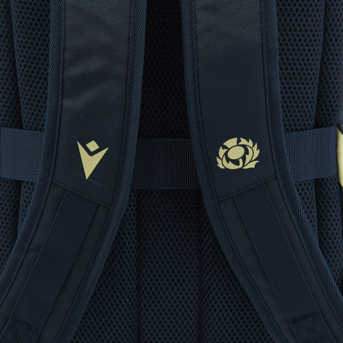 Close-up of the navy shoulder straps with mesh padding on the Scotland SRU 26/27 Backpack by Macron, featuring two yellow logos—one chevron-shaped and one circular with a stylized thistle—that highlight its distinctive design.
