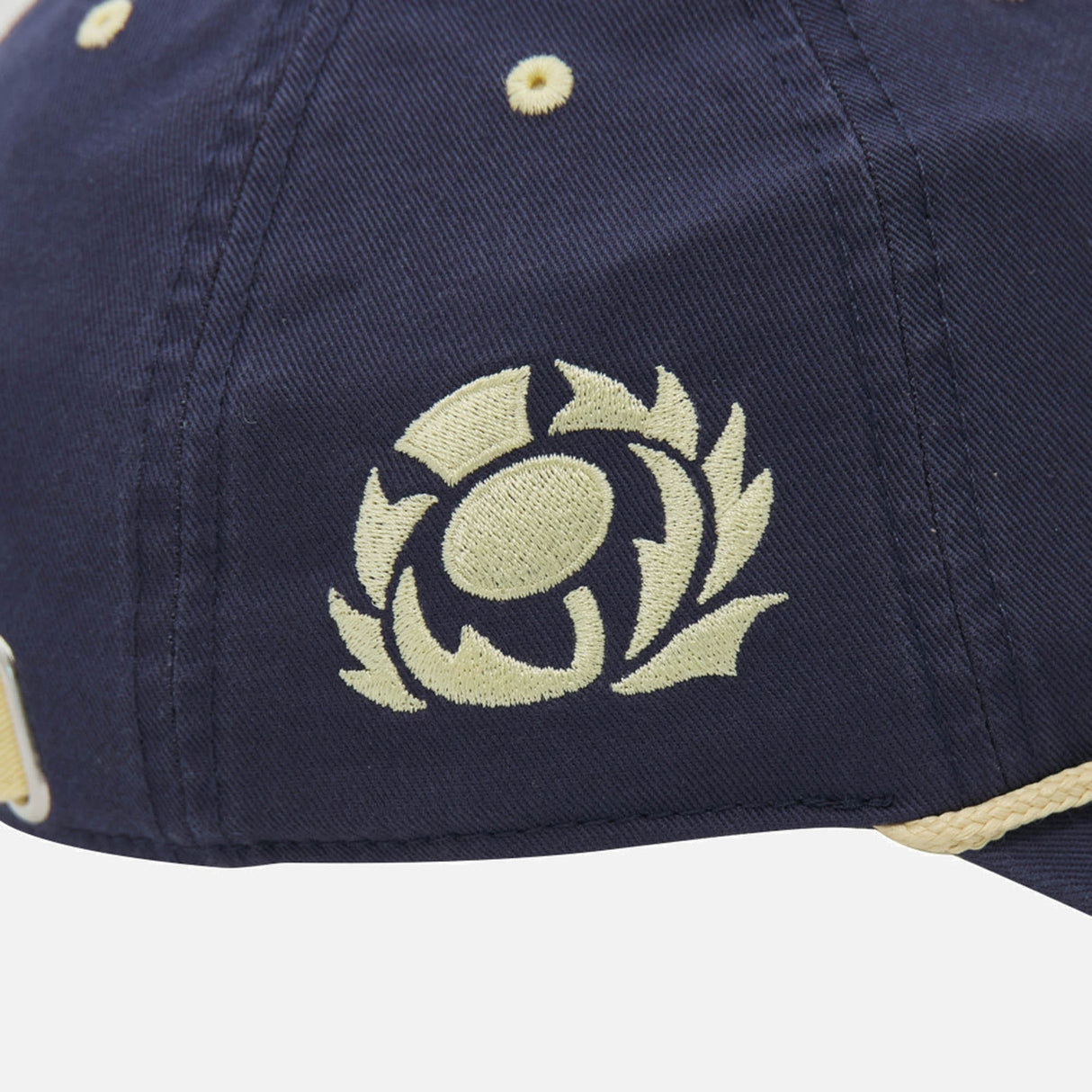 The Scotland SRU 26/27 Dad Cap by Macron is a navy blue cap styled in the classic Macron Baseball Cap design, featuring a yellow embroidered floral emblem with leaf motifs on the side and marked with SRU 26/27.