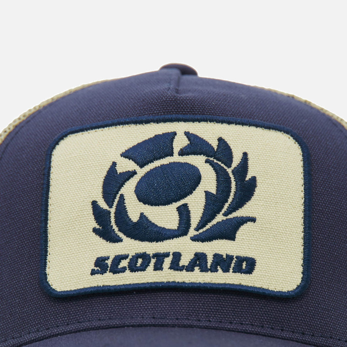 Close-up of the Scotland SRU 26/27 Trucker Cap by Macron, featuring a patch with a stylized rugby ball logo and "Scotland" embroidered in blue.