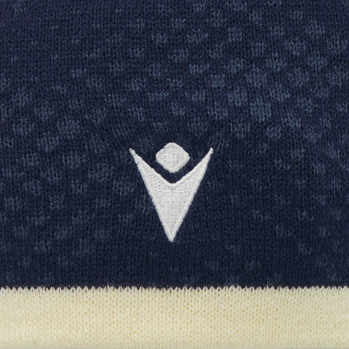 Close-up of the Scotland SRU 26/27 Knit Beanie by Macron, featuring a navy blue knitted fabric with a white geometric logo and a beige stripe at the bottom, highlighting the premium detailing of this official Scotland Rugby beanie.