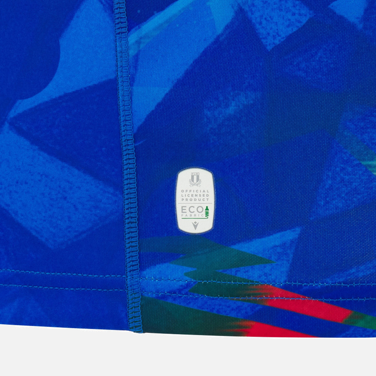 Close-up of the Italy 26/27 Home Replica Jersey by Macron, featuring blue geometric patterns, visible stitching, and an “Official Licensed Product” eco-friendly label near the seam. This jersey from Macron exemplifies quality craftsmanship and attention to detail.