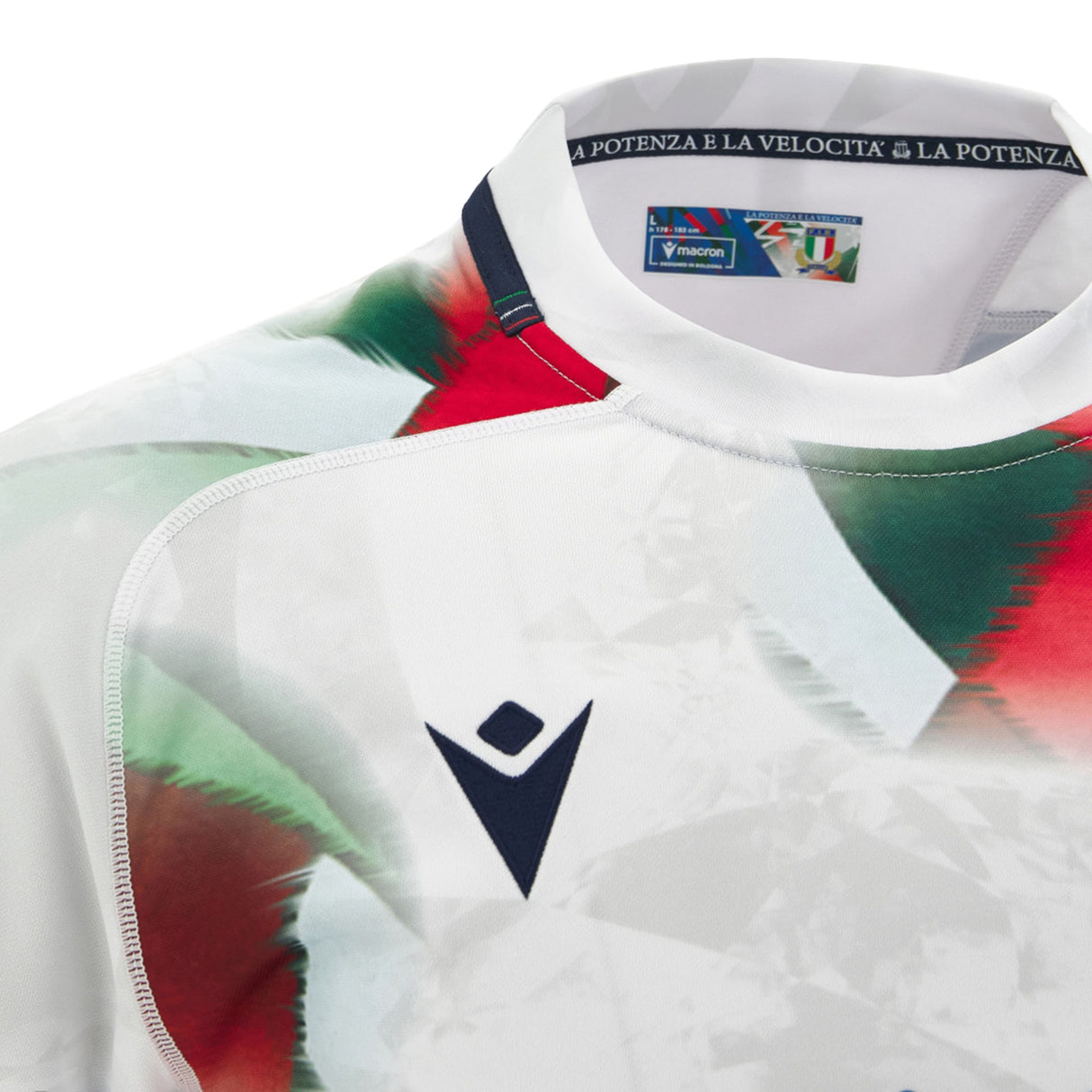 Close-up of the Italy 26/27 Away Replica Jersey by Macron, featuring abstract green and red patterns on a crisp white base, a navy Macron logo, and a collar lined with Italian flag details and inner text.