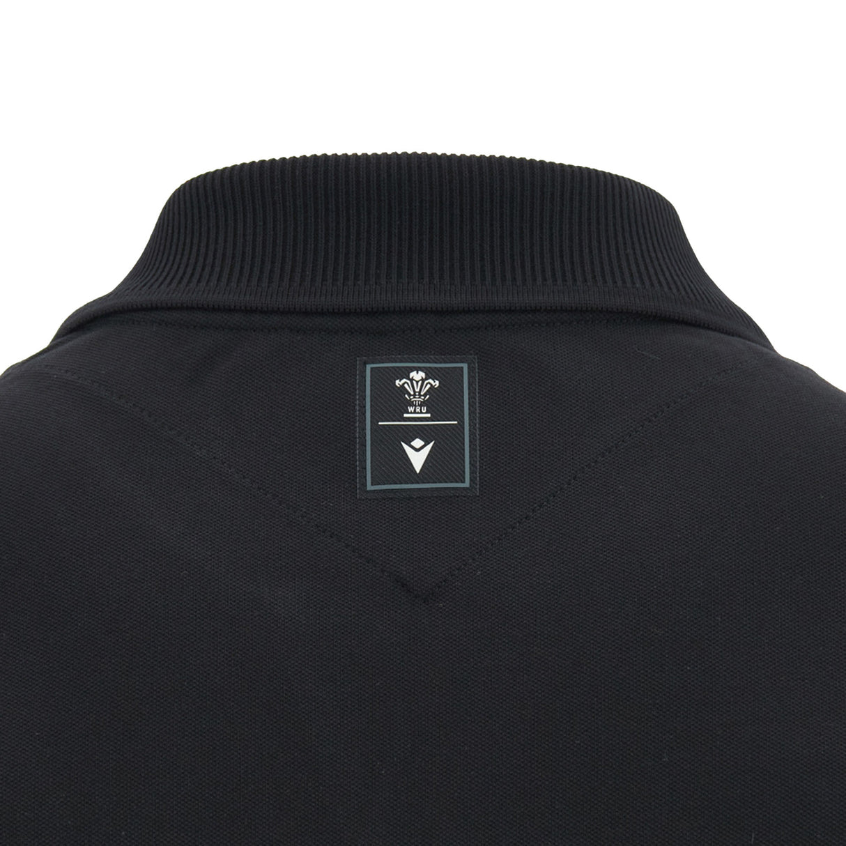 Close-up of the back collar of the black Wales WRU 26/27 Travel Cotton Polo by Macron, featuring a small rectangular label with a crown and chevron design.