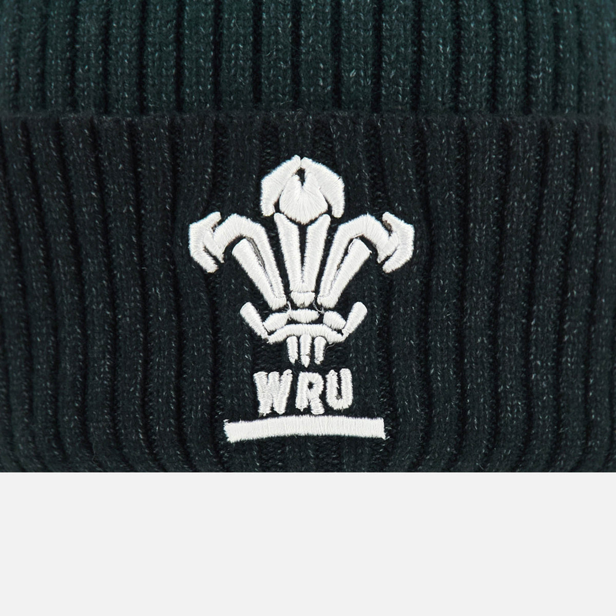 A close-up of the Wales WRU 26/27 Pom-Pom Beanie by Macron, a black ribbed knit beanie featuring the white embroidered Welsh Rugby Union (WRU) logo.