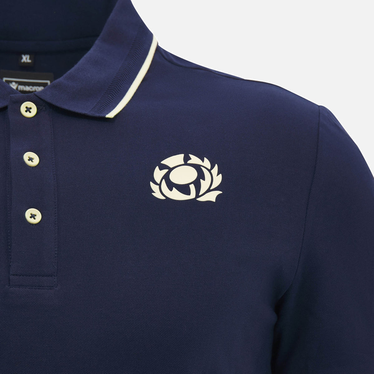 Close-up of the Scotland SRU 26/27 Travel Polo by Macron in navy, featuring cream buttons and a white rugby thistle emblem on the left chest.