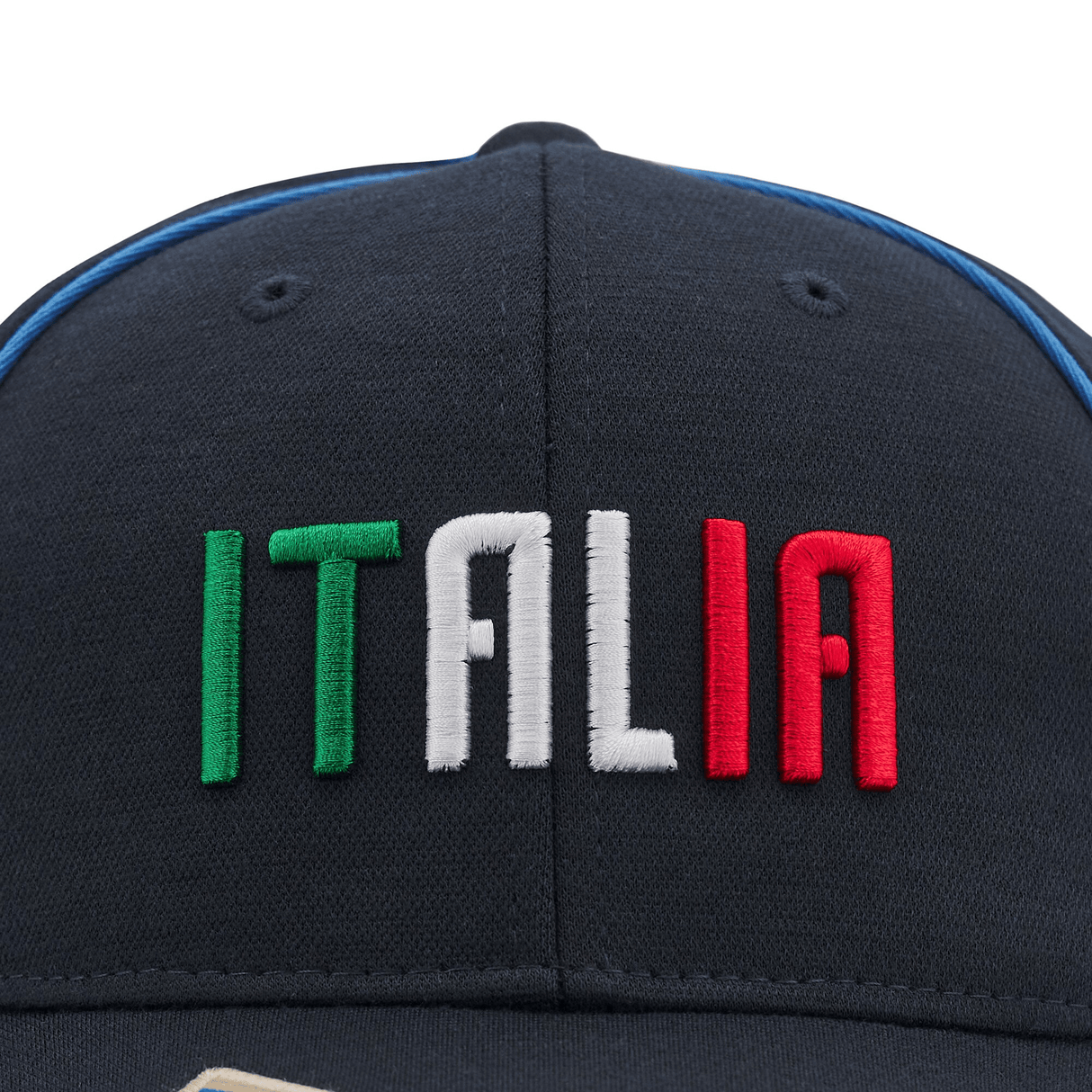 A close-up view of the Italy Curved Visor Cap 24/25 by Macron showcases "ITALIA" embroidered in green, white, and red letters against a navy blue background.