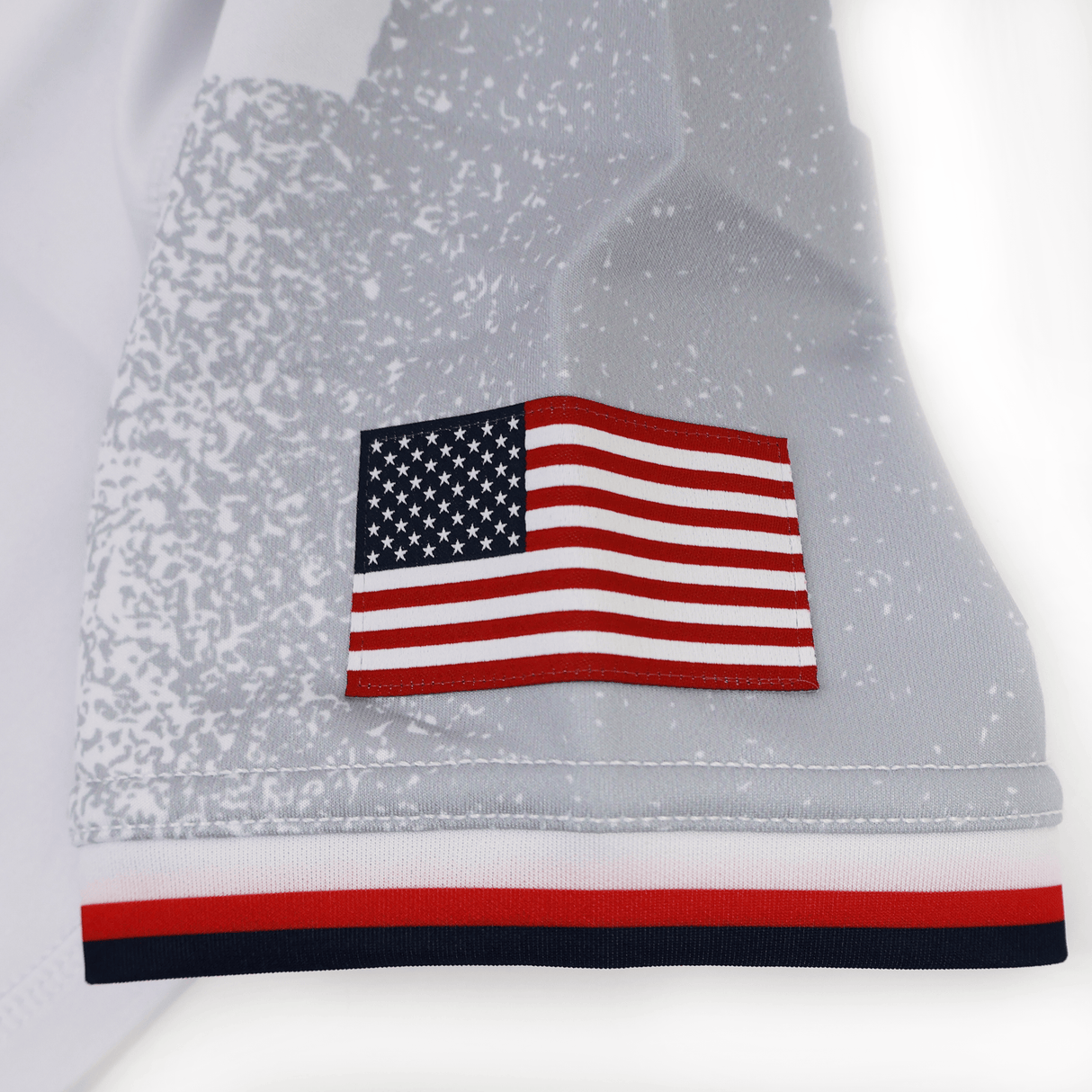 Close-up of the Women's USA Rugby 24/25 Away Body Fit Jersey by Macron, showing a printed American flag and a red, white, and blue striped trim along the edge.