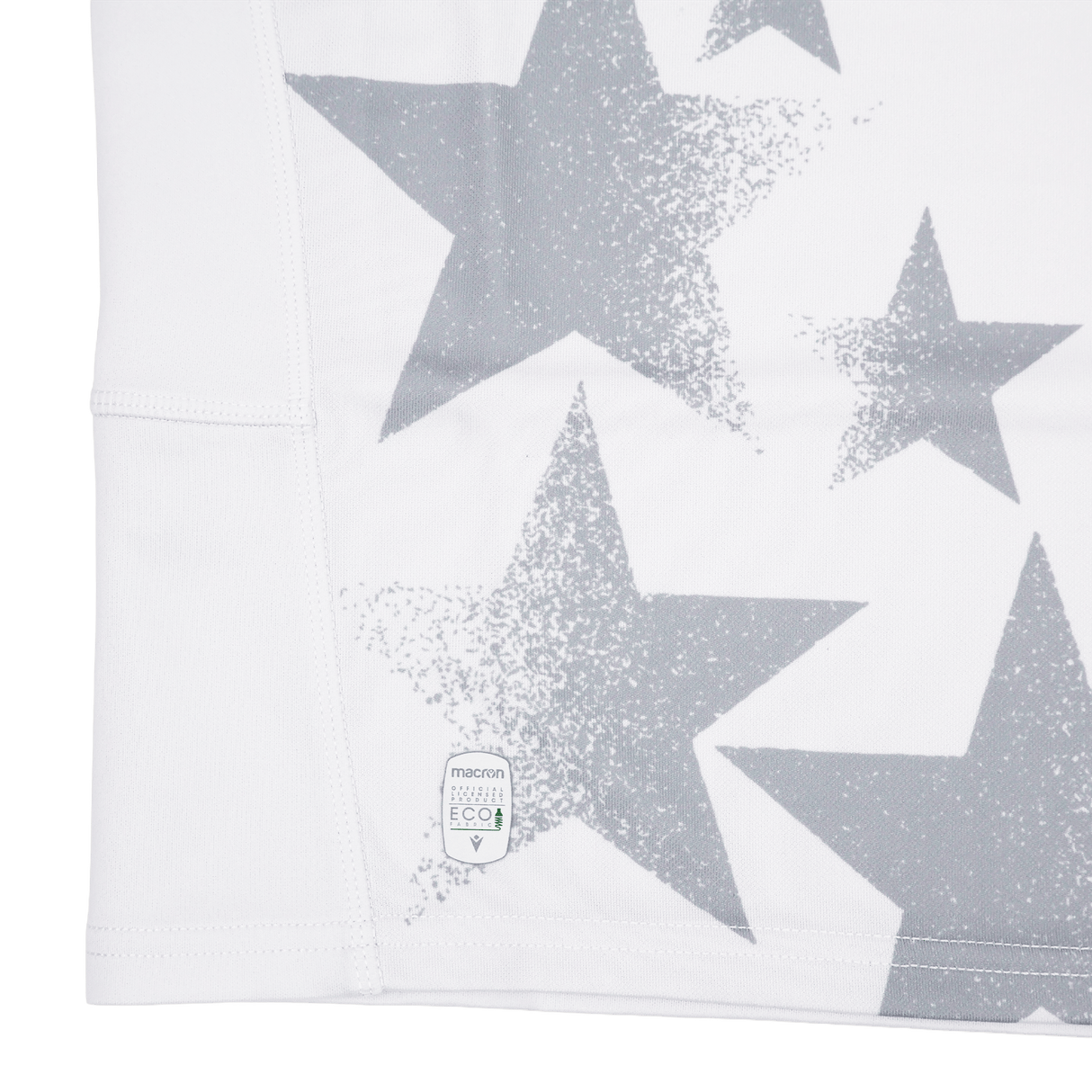 Close-up of white fabric with large and small gray stars, like the Youth USA Rugby 24/25 Away Jersey by Macron, featuring a small eco-friendly label near the hem.