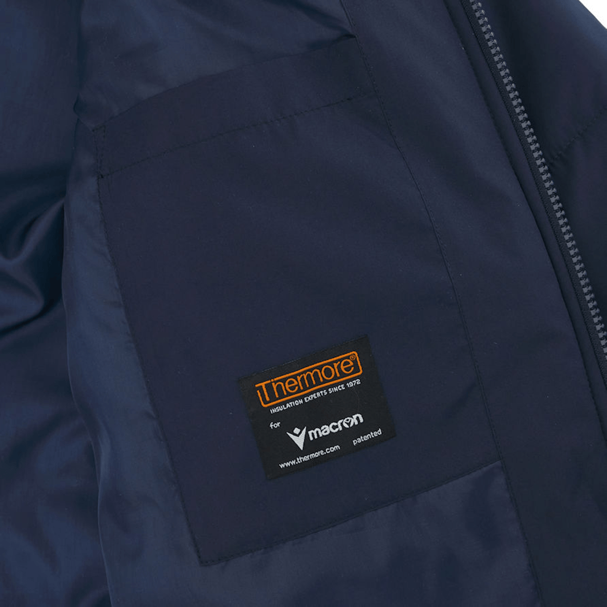 Close-up of the USA Rugby 25 Padded Bench Jacket by Macron in navy blue, featuring two internal pockets. One pocket shows a black label with orange and white text, indicating "Thermore" and "Macron," the official supplier for USA Rugby.
