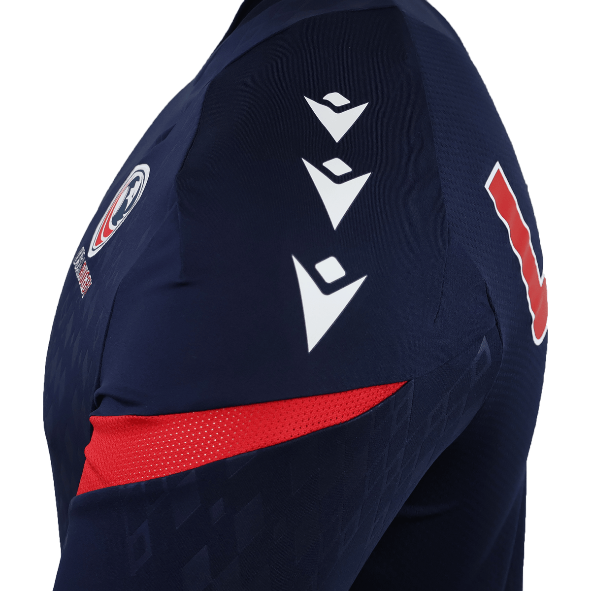 Close-up of the USA Rugby 25/26 LS Training Poly Shirt by Macron: a navy long sleeve jersey with three white shoulder chevrons, chest logo, red accents, and a bold red and white "L" on the sleeve.