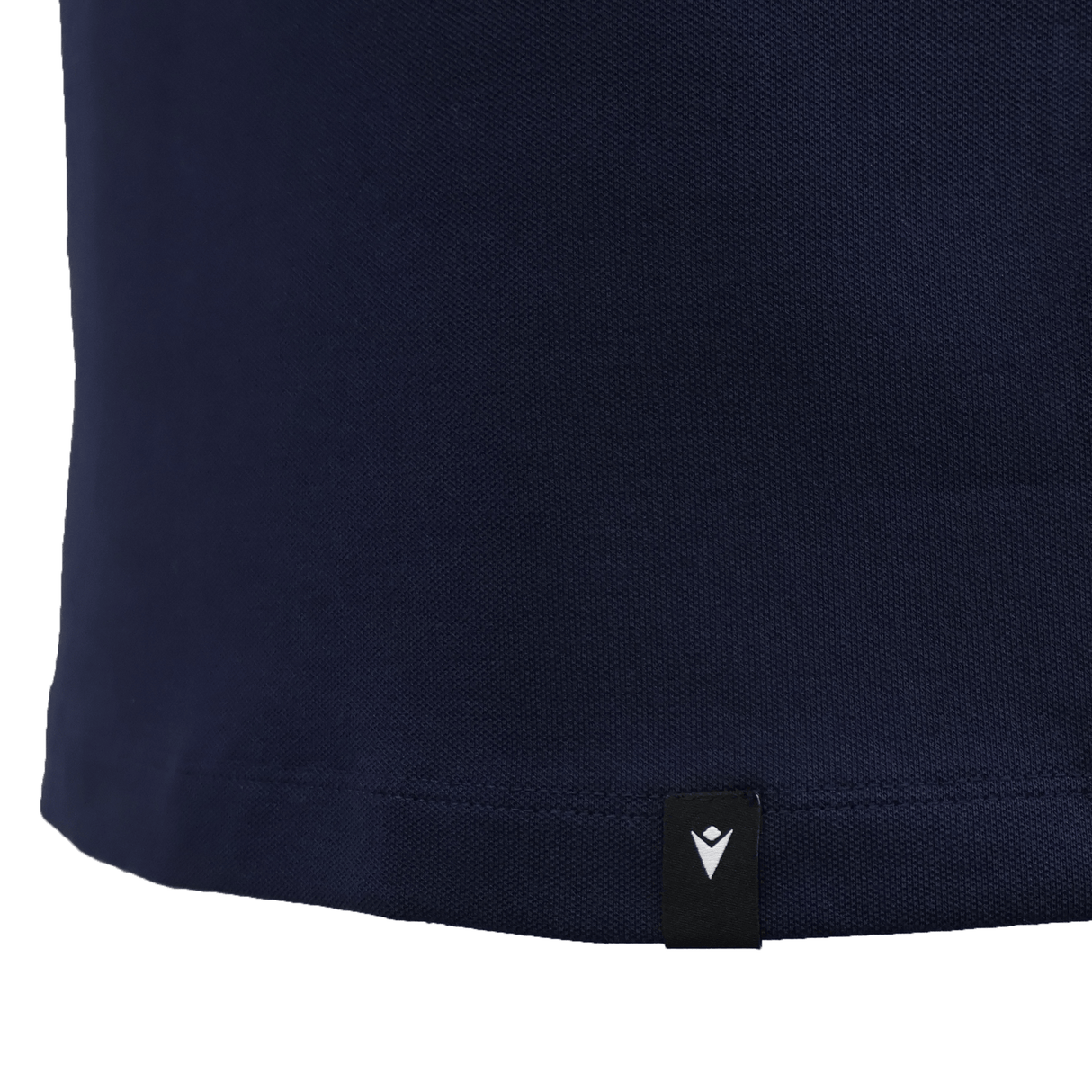 Close-up of the lower part of the USA Rugby 25/26 Athleisure Cotton Polo by Macron in navy blue, showing a small black tag with a white logo near the hem.
