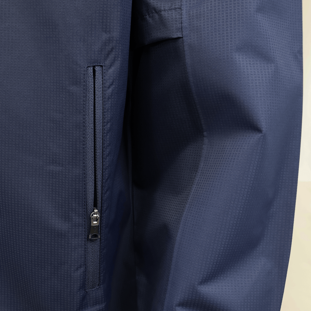 Close-up of the USA Rugby 25/26 Rain Jacket by Macron in navy blue, showing a zippered sleeve pocket and textured waterproof fabric—ideal for staying dry during intense matches.