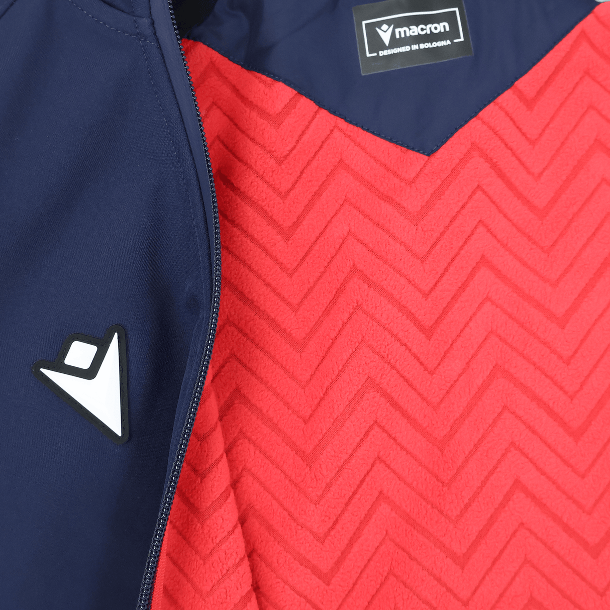 Close-up of the USA Rugby 25/26 Athleisure Softshell Jacket by Macron, navy blue and partially unzipped to show a red zigzag inner lining with visible logo—an ideal water-resistant jacket for athleisure style.