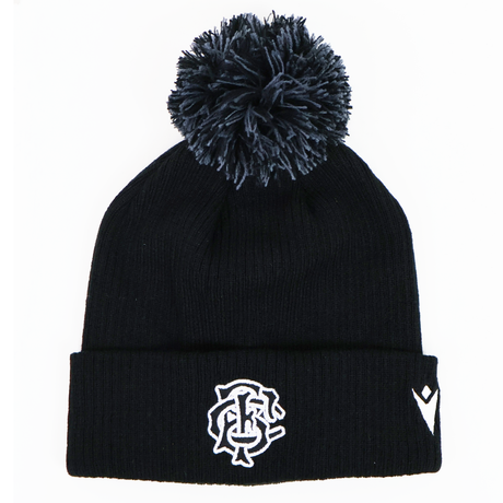 The Barbarians 25/26 Pom-Pom Beanie by Macron features a black knit design with a white embroidered monogram logo and emblem on the cuff, inspired by the classic Barbarians beanie.