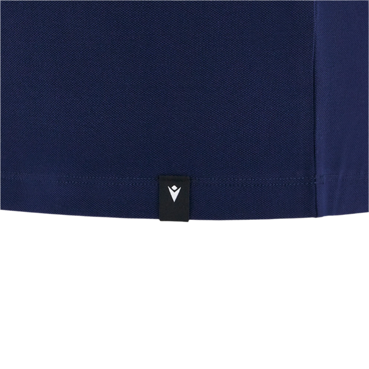 Close-up of the hem of the Scotland 25/26 Player Travel Cotton Polo by Macron, dark blue in color, featuring a small black tag with a white logo attached to the seam.