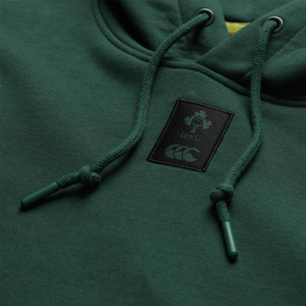 Close-up of the Ireland 26 Leisure Hoodie by Canterbury, featuring a dark green design with a logo patch displaying a shamrock, “IRFU,” and a stylized animal—this leisure hoodie is perfect for fans who value comfort and team spirit.