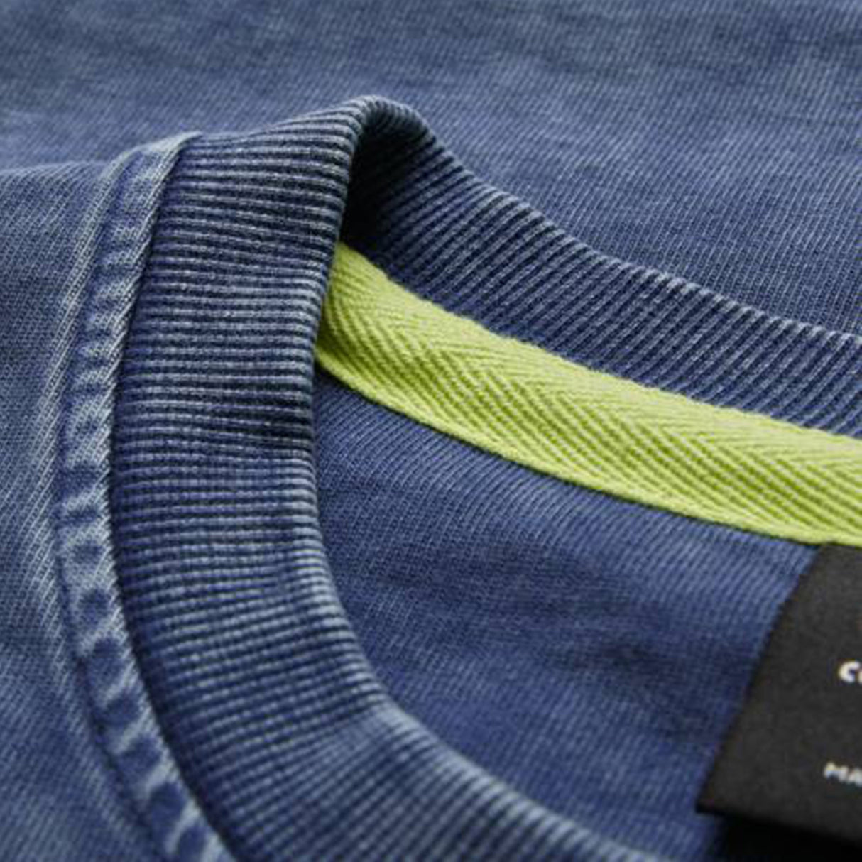 Close-up of the Ireland 26 Premium OS Washed T-shirt by Canterbury in blue acid-wash cotton, showcasing the ribbed collar, lime green interior neck tape, and a black Canterbury brand label. This t-shirt features an oversized fit for enhanced comfort and contemporary style.