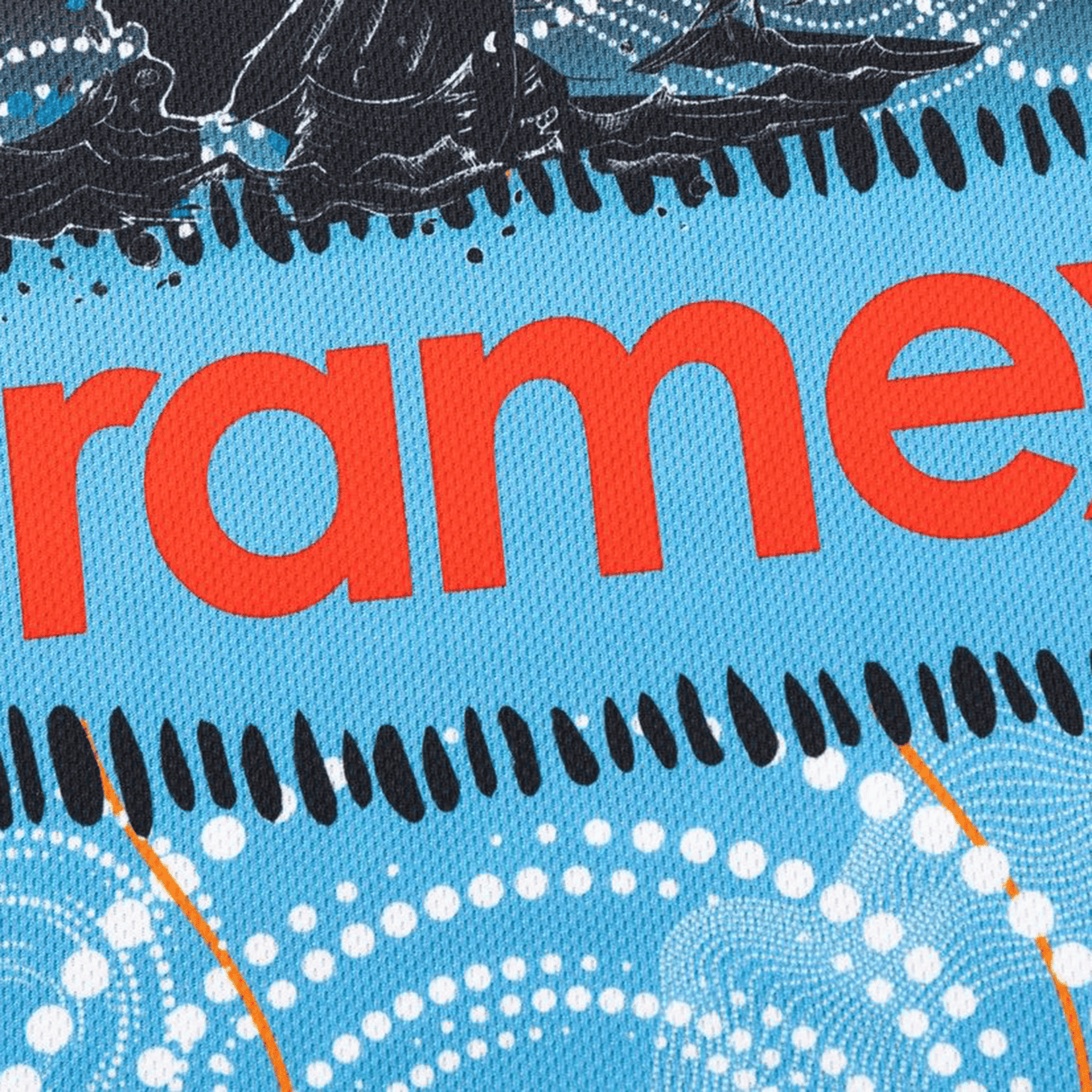Close-up of a blue textured surface from the Sharks Indigenous NRL 25/26 Replica Jersey by Classic Sportswear, featuring aboriginal-style white dot patterns and partial red "ramex" text.