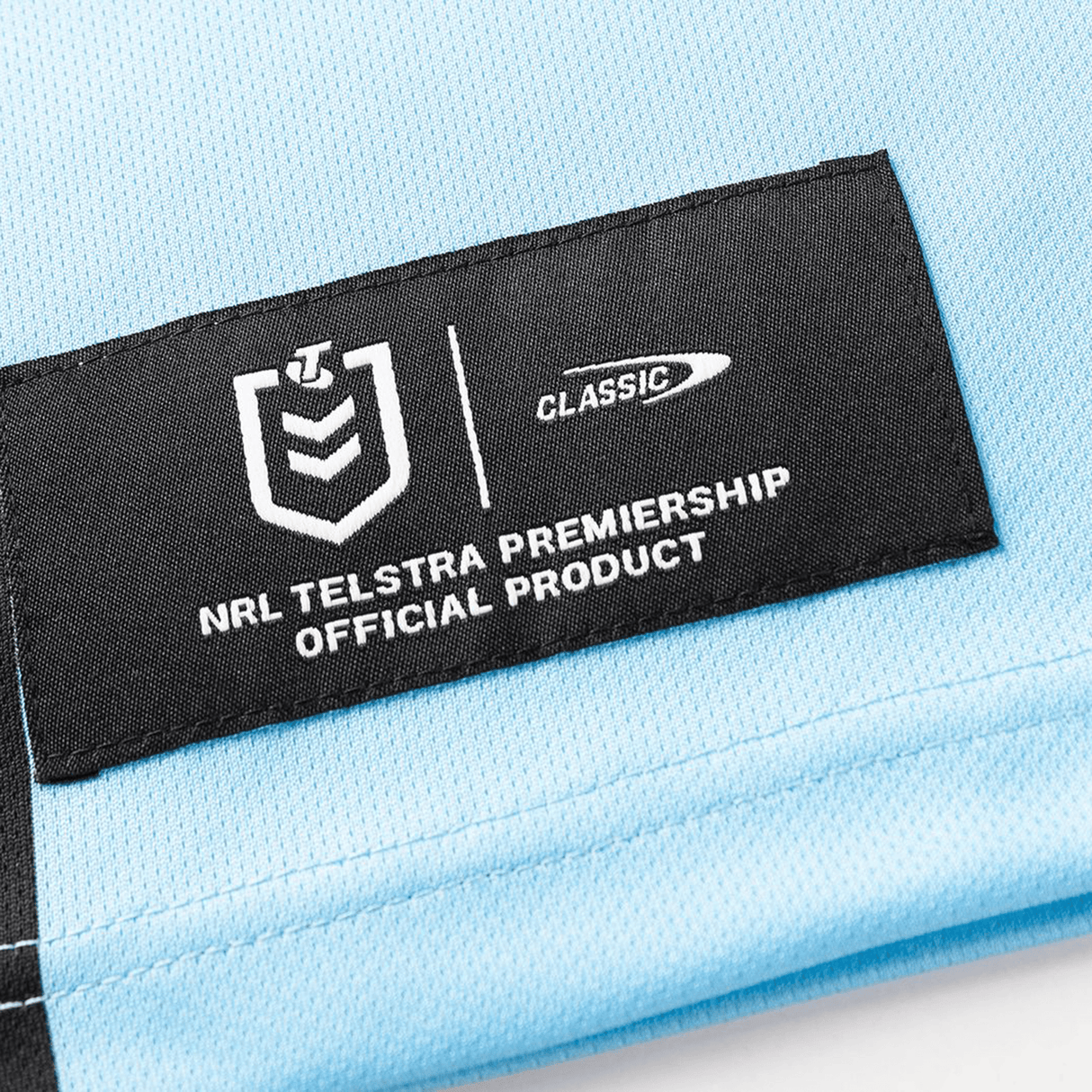 A close-up of the black label on the Sharks NRL 26/27 Replica Home Jersey by Classic Sportswear shows the NRL Telstra Premiership logo and "NRL Telstra Premiership Official Product" for dedicated Sharks fans.