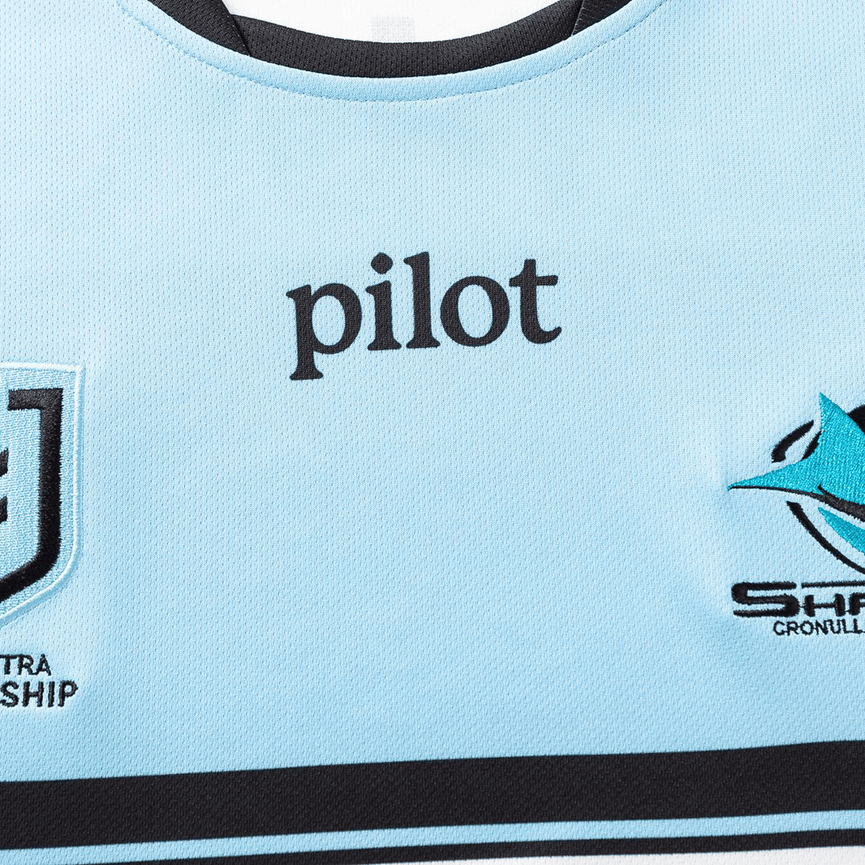Close-up of a Sharks NRL 26/27 Replica Home Jersey by Classic Sportswear in light blue, featuring "pilot" in black and two logos on each side of the chest.