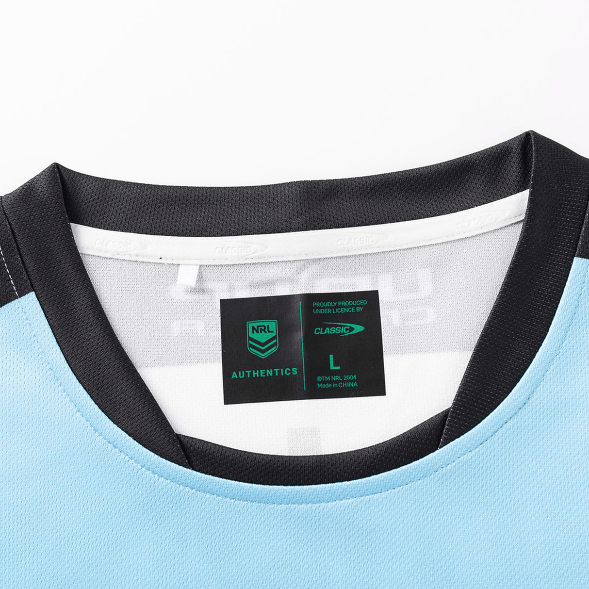 Close-up of the neckline and label of the Sharks NRL 26/27 Replica Home Jersey by Classic Sportswear in light blue with black trim, featuring size L, Classic Sportswear branding, and care info.