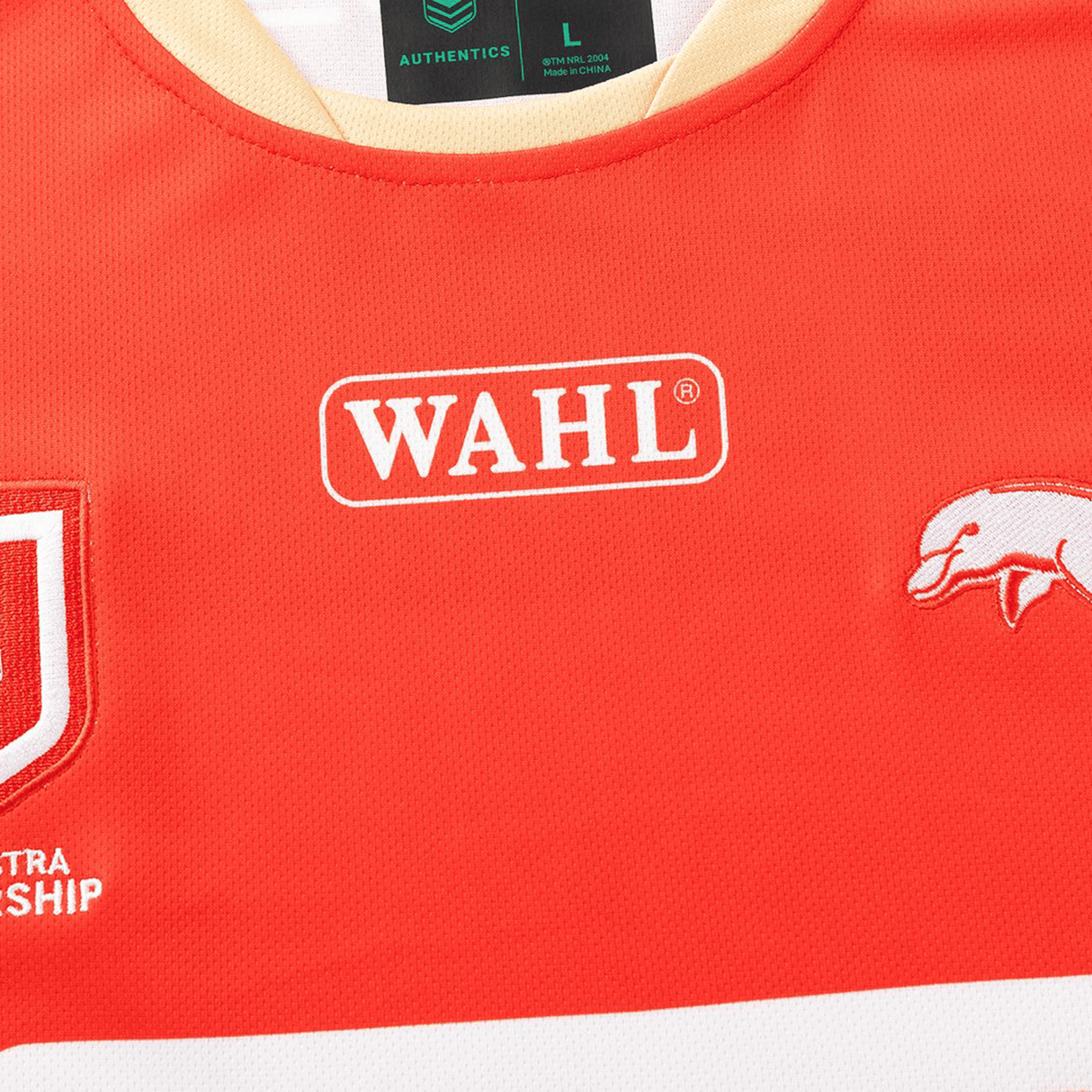 Close-up of the Dolphins NRL 26/27 Replica Home Jersey by Classic Sportswear, showing a red design with WAHL logo, stylized white animal graphic, Classic Sportswear branding, and partial logos.