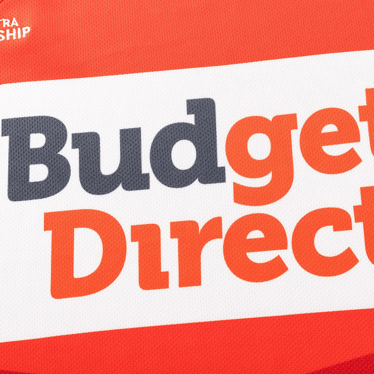 Close-up of a red and white "Budget Direct" sign, like the logo featured on the Dolphins NRL 26/27 Replica Home Jersey by Classic Sportswear.