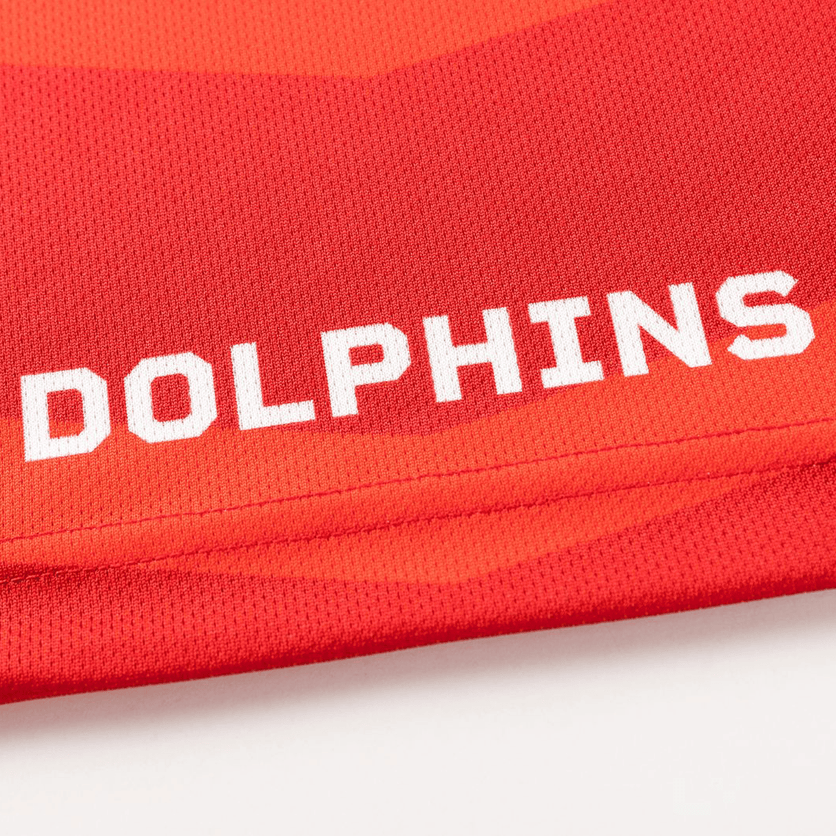 Close-up of red fabric from the Dolphins NRL 26/27 Replica Home Jersey by Classic Sportswear, showing "DOLPHINS" in bold white capitals.