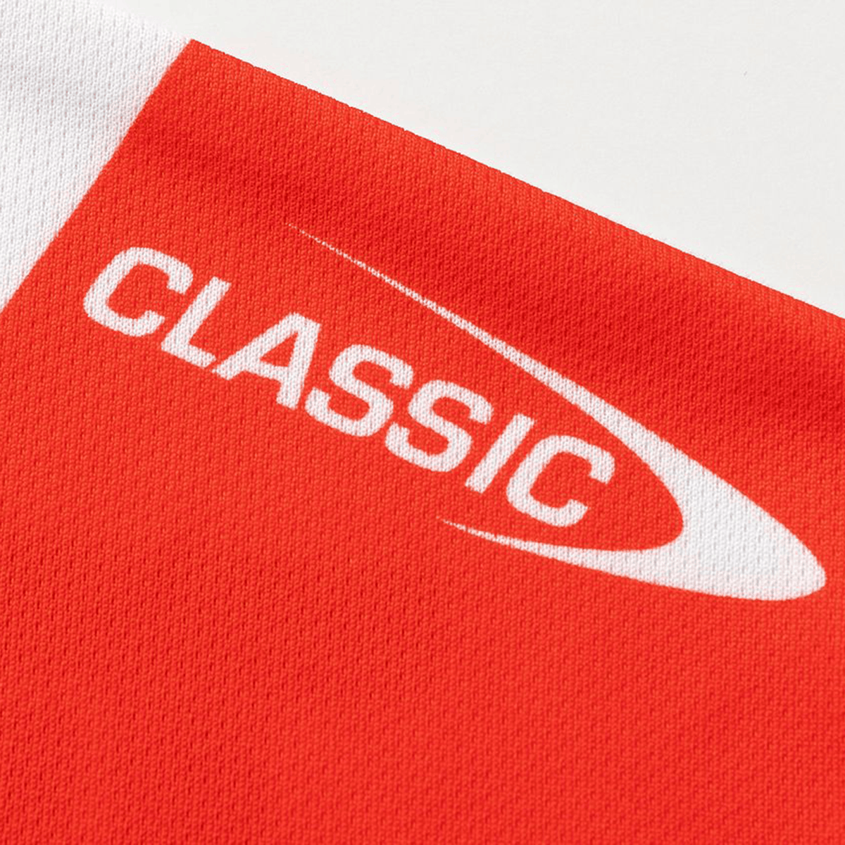 A close-up of the Dragons NRL 26/27 Replica Home Jersey by Classic Sportswear shows red fabric with a white "CLASSIC" logo and curved design, showcasing the quality and detail of this Classic Sportswear rugby jersey.