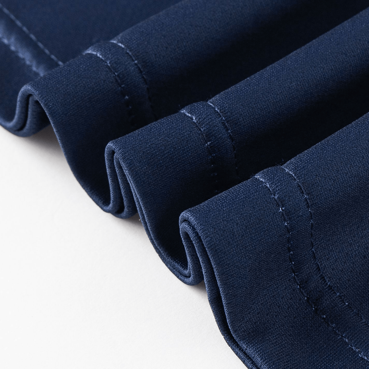 A close-up of the neatly folded Highlanders Super Rugby Team Polo 25/26 by Classic Sportswear, in navy blue, displays its visible stitching and moisture-wicking fabric against a white background.