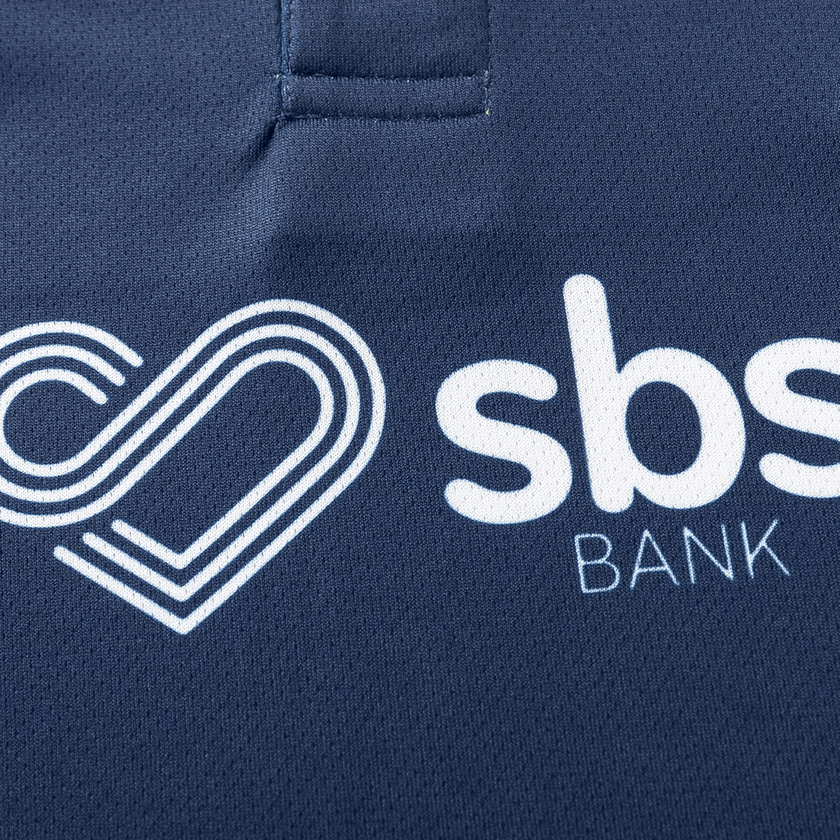 Close-up of a navy Highlanders Super Rugby Team Polo 25/26 by Classic Sportswear, featuring a moisture-wicking fabric and a white logo with a stylized heart and "SBS Bank," proud partner of the team.