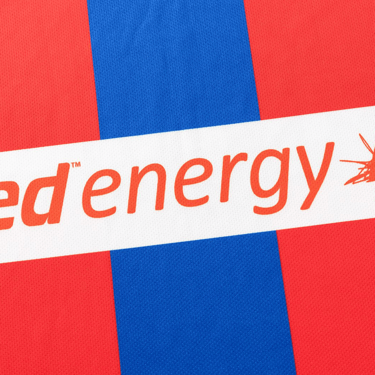 Close-up of the Knights NRL 26/27 Replica Home Jersey by Classic Sportswear, featuring red and blue stripes and partially visible "energy" text in orange on the fabric.