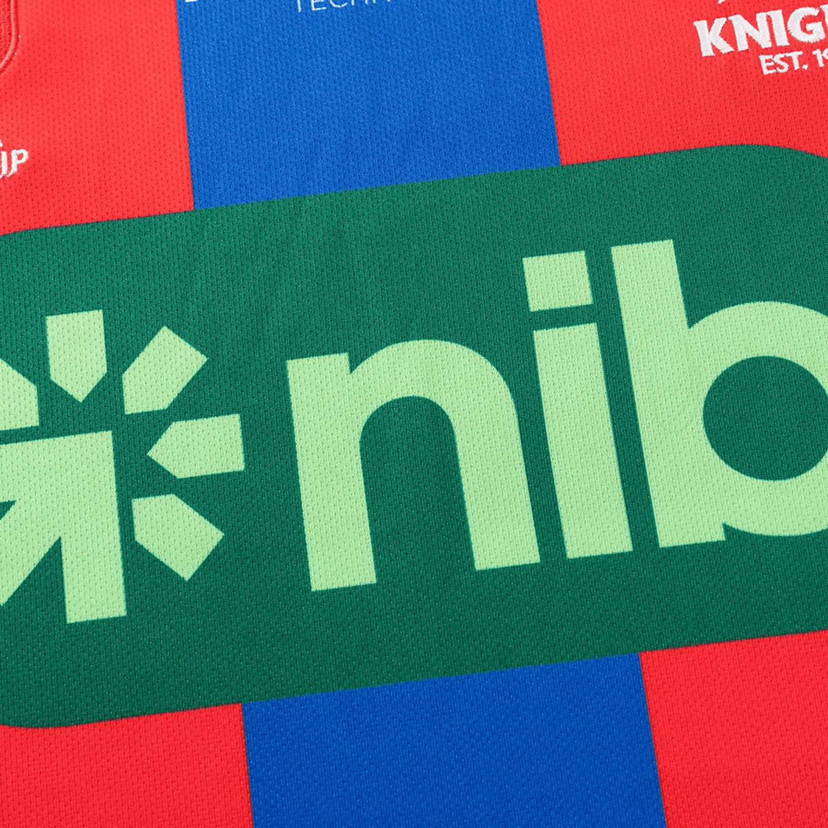 A close-up of the Knights NRL 26/27 Replica Home Jersey by Classic Sportswear in red and blue, featuring a green "nib" sponsor logo on the chest, highlights this authentic high-performance sportswear.