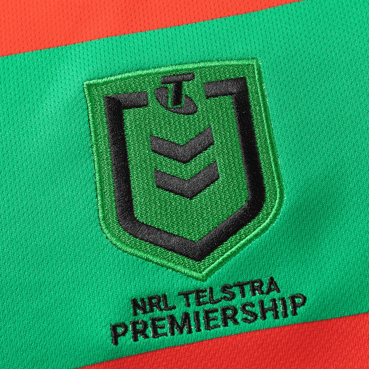 The Rabbitohs NRL 25/26 Replica Home Jersey by Classic Sportswear features an embroidered NRL Telstra Premiership logo on a red and green fabric background, embodying the essence of a Rabbitohs Jersey.
