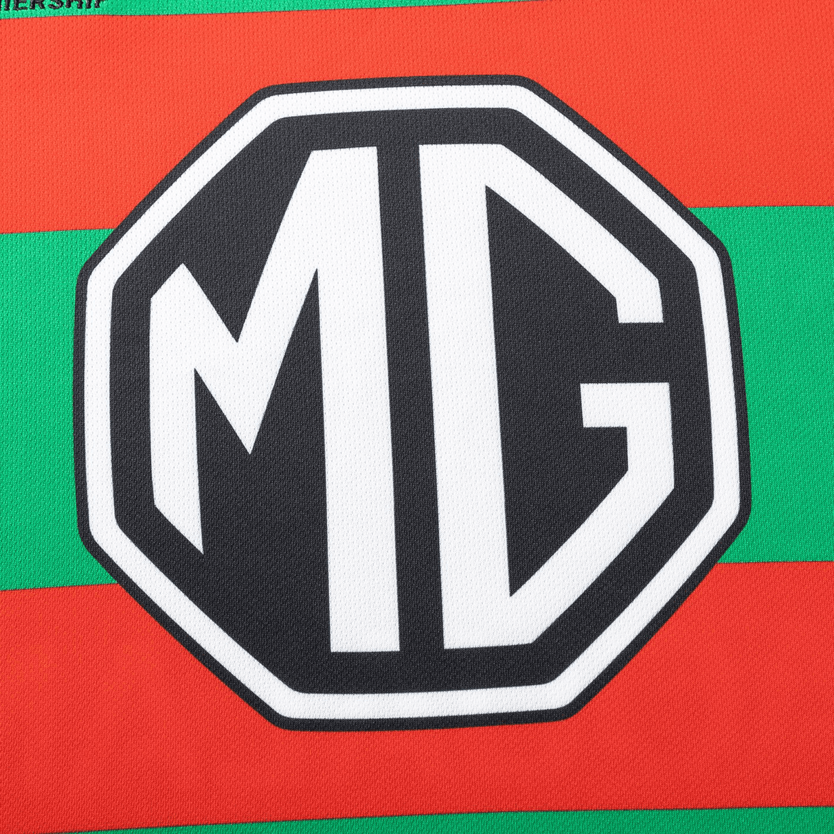 Close-up of the Classic Sportswear logo with "MG" in bold white outlined in black, set against red and green stripes emulating a Rabbitohs NRL 25/26 Replica Home Jersey by Classic Sportswear.